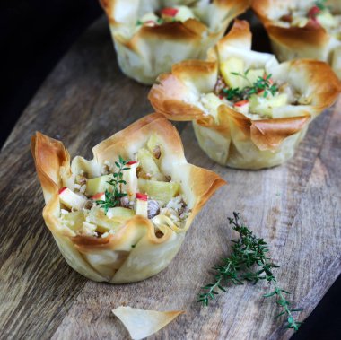 Tahta arka planda gorgonzola, elma ve cevizle dolu Phyllo hamur işi sepetleri. Genel Görünüm.