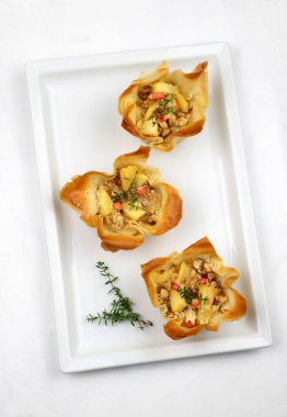 Beyaz bir tabakta Gorgonzola, elma ve cevizle dolu Phyllo hamur işi sepetleri. Noel ışıkları süslemesi. Tatil sezonu. Tam üstte.