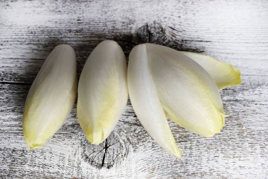 Taze çiğ Belçika hindibaları (hindiba) ahşap bir arka planda izole edilmiş. Sağlıklı ve vejetaryen yemekleri. Tam üstte.