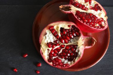 Siyah arka planda izole bir tabakta ikiye bölünmüş taze olgun nar. Sağlıklı bir yaşam tarzı. Genel Görünüm.