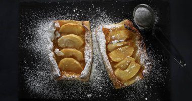 Arkaplanda krema serpiştirilmiş elmalı turta..