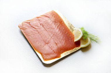 İnce dilimlenmiş tütsülenmiş somon, limon dilimleri ve beyaz arka planda izole edilmiş taze dereotuyla süslenmiş. Deniz ürünleri. Genel Görünüm.