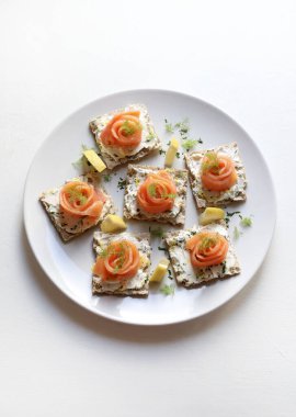 Smoked salmon and cream cheese canapes on wholemeal crackers, garnished with dill and lemon, on a white background. Christmas and holiday season. Overhead view.