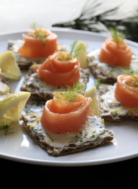 Tütsülenmiş somon ve krem peynirli kanatlar beyaz tabakta dereotlu ve limonlu krakerler. Noel ve tatil sezonu.
