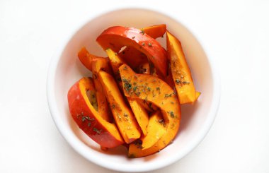 Taze kekik ile baharatlı balkabağı dilimleri ve beyaz arka planda pişirilmeye hazır beyaz bir kasede ekstra bakire zeytin yağı. Kış garnitürü. Sağlıklı ve vejetaryen yemekleri. Genel Görünüm.