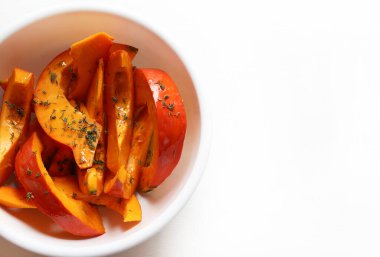 Taze kekik ile baharatlı balkabağı dilimleri ve beyaz arka planda pişirilmeye hazır beyaz bir kasede ekstra bakire zeytin yağı. Kış garnitürü. Sağlıklı ve vejetaryen yemekleri. Genel Görünüm.