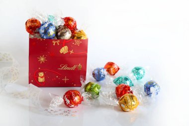 Floransa, İtalya, 8 Aralık 2025. Lindt Lindor İsviçre çikolatalarının olduğu Noel kutusu beyaz arka planda çeşitli aromalı trüf mantarları. Renkli çikolata paketleri. Noel ve tatil sezonu.