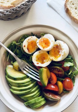Akdeniz salatası, avokado ile haşlanmış yumurta, kremalı yumurta ve roket yatağında vişneli domates, EVO yağı, tuz ve limon suyu. Tek ve dengeli tabak.