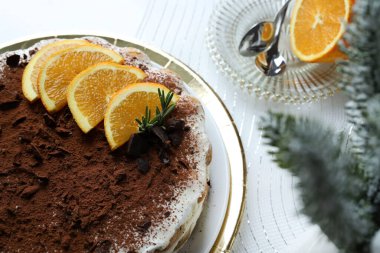 Lezzetli çikolata ve portakallı tiramisu keki, kakao ve çikolata parçalarıyla tozlanmış, portakal dilimleri ve biberiye ile süslenmiş, altın tepsiye konmuş beyaz bir tabakta servis ediliyor. Noel süsü. İtalyan tatlısı.