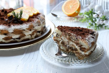 Lezzetli çikolata ve portakallı tiramisu keki, kakao ve çikolata parçalarıyla tozlanmış, portakal dilimleri ve biberiye ile süslenmiş, altın tepsiye konmuş beyaz bir tabakta servis ediliyor. Noel süsü. İtalyan tatlısı.