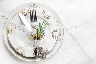 Noel ya da yeni yıl sofrası için mükemmel bir dekor, altın çiçekli beyaz tabaklar, şeffaf bir kurdeleyle sarılmış eski usul saplı çatal bıçaklar ve taze bir çam filizi. Beyaz arkaplan.