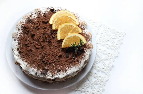 Çikolata ve portakallı tiramisu keki, kakao ve çikolata parçalarıyla tozlanmış, portakal dilimleri ve biberiye ile süslenmiş, beyaz arka planda izole edilmiş beyaz bir tabakta servis ediliyor. İtalyan tatlısı. Genel Görünüm.