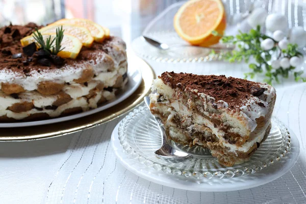 Lezzetli çikolata ve portakallı tiramisu keki, kakao ve çikolata parçalarıyla tozlanmış, portakal dilimleri ve biberiye ile süslenmiş, altın tepsiye konmuş beyaz bir tabakta servis ediliyor. Noel süsü. İtalyan tatlısı.