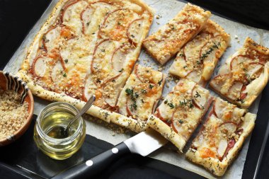 Peynirli, ince dilimlenmiş armut dilimlenmiş, ceviz serpiştirilmiş ve taze kekik ve bal ile süslenmiş tuzlu puf böreği. Turtanın yanında bir kase doğranmış ceviz ve bir kavanoz bal var..