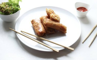 Kızarmış Çin börekleri (Çin dürümleri), yemek çubukları, kırmızı sos ve beyaz arka planda taze marul ile servis edilir. Tipik Asya mutfağı..