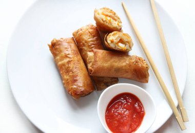 Beyaz zemin üzerinde çubuklar ve kırmızı sosla servis edilen kızarmış böreklerle (Çin ruloları) kaplı tabak. Tipik Asya mutfağı..