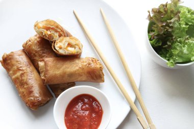 Kızarmış Çin börekleri (Çin dürümleri), yemek çubukları, kırmızı sos ve beyaz arka planda taze marul ile servis edilir. Tipik Asya mutfağı..