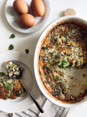 Yanında porsiyon servis edilen taze pişmiş sebzeli frittata ile birlikte beyaz bir fırın tabağı. Sol üste üç tam yumurta. Yukarıdan görüntüle.