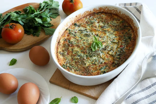 Taze pişmiş sebzeli omlet ile pişirme kabı, onu hazırlamak için taze malzemelerle çevrili..