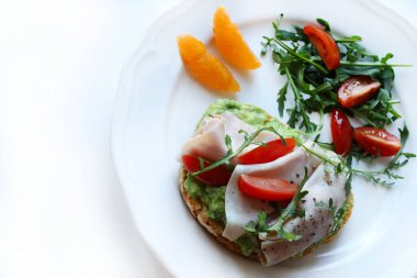 Fırında ekmek, avokado kremalı bruschetta, pişmiş jambon ya da hindi, ikiye bölünmüş kiraz domatesli, zeytinyağlı, taze roketli ve mandalinli ya da portakallı. Beyaz arkaplan.