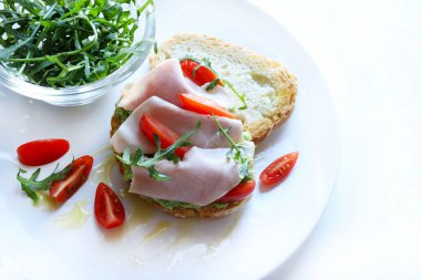 Fırında ekmek, avokado kremalı bruschetta, pişmiş jambon ya da hindi, ikiye bölünmüş kiraz domatesli, zeytinyağlı, taze roketli ve mandalinli ya da portakallı. Beyaz arkaplan.