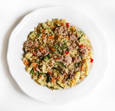 Ton balıklı kuskus ve beyaz arka planda havuç, kabak, biber, bezelye ve taze maydanoz gibi pişmiş sebzeler. Sağlıklı, vejetaryen ve vejetaryen yemekleri. Tam üstte.