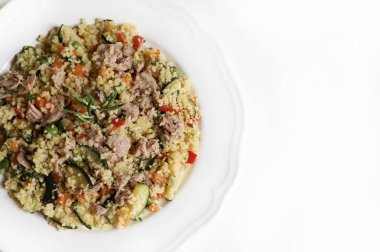 Ton balıklı kuskus ve beyaz arka planda havuç, kabak, biber, bezelye ve taze maydanoz gibi pişmiş sebzeler. Sağlıklı, vejetaryen ve vejetaryen yemekleri. Tam üstte.