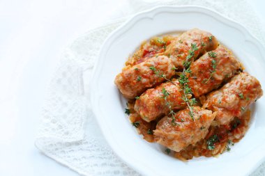 Beyaz arka planda taze kekik yapraklarıyla kaplı, et ve pirinç dolgulu beyaz lahana rulosu. Geleneksel bir kış yemeği. Sarma, sarmaşık, holubtsi, dolmades.