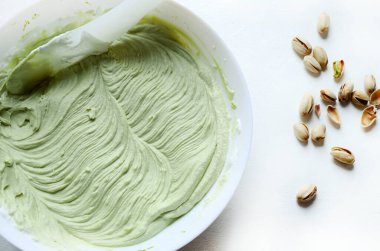 Beyaz bir yüzeye serpiştirilmiş birkaç kabuklu ve kabuksuz şam fıstıklı silikon spatulayla karıştırılmış ev yapımı şam fıstığı kreması. Mutfak yaratımı ve ev işçiliği kavramı.