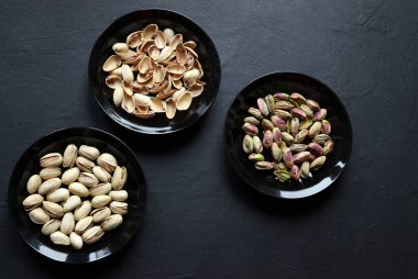 Üç siyah şam fıstığı kasesi, biri kabuklu şam fıstığı, biri kabuklu şam fıstığı, ve biri de boş kabuklu, siyah arka planda izole edilmiş. Sağlıklı, vejetaryen kurutulmuş meyve. Genel Görünüm.