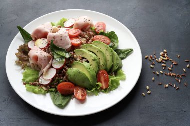 Avokadolu taze ve sağlıklı karışık tahıl salatası dilimlenmiş hindi ya da tavuk, kiraz domatesleri, turp taze marul yaprakları ve bebek ıspanağı, siyah arka planda. Genel Görünüm.