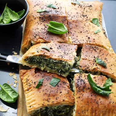 Spanakopita, siyah bir zemin üzerinde fillo hamur işi, taze ıspanak ve beyaz peynirle yapılan geleneksel bir Yunan turtası. Yunan mutfağı. Genel Görünüm.