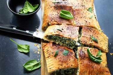 Spanakopita, siyah bir zemin üzerinde fillo hamur işi, taze ıspanak ve beyaz peynirle yapılan geleneksel bir Yunan turtası. Yunan mutfağı. Genel Görünüm.