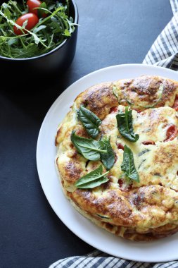 Çeri domatesli fırında frittata ve koyu arkaplanda taze ıspanak. Yaz yemeği. Genel Görünüm.