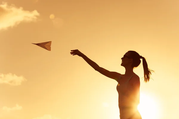 Silhueta de mulher jovem jogando avião de papel — Fotografia de Stock