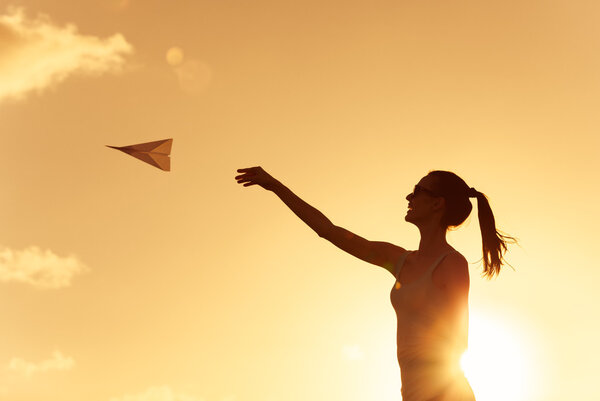 Silhouette of young woman throwing paper airplane