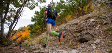 Sıkışan çoraplar ve su dolu sırt çantası giyen sporcu dağda sonbahar maratonu yapıyor.
