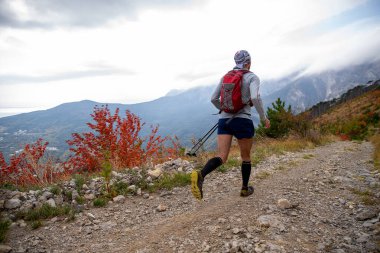 Elinde yürüyüş direkleri olan erkek sporcu dağ maratonunda koşuyor.