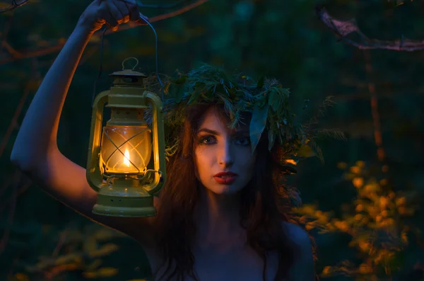 Mooi meisje houdt een lantaarn met een kroon op zijn hoofd staat alleen in het bos. Heks verlicht uw manier. Halloween. Stockfoto