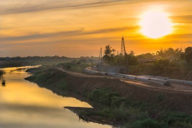 Bir kazık sürücüsü, turuncu gökyüzünde bir inşaat alanında çalışıyor..