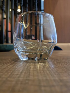 Masanın üzerinde boş, berrak bir cam bardak taklacısı duruyor, el değmemiş yüzeyi çevredeki ışığı yansıtıyor.