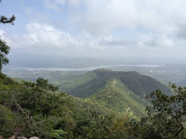 Manzaralı dağ manzarası yoğun yeşillik, bulutlu gökyüzü ve muson mevsiminde yüksek bir görüş noktasından görülebilen uzak kasaba..