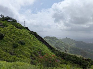 Gökyüzü bulutlu muson yağmurlarına karşı inşa edilmiş, uçuruma konmuş, haberleşme kuleleri olan yeşil bir tepe manzarası..