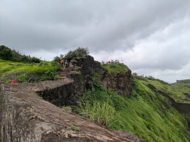 Sinhagad Kalesi 'nde bulutlu bir muson yağmuru altında yemyeşil tepelerle çevrili popüler bir bakış açısına giden manzaralı bir taş yol..