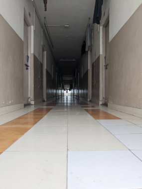 Kapalı bir koridor, fayanslı döşemeler, boyanmış duvarlar ve sonunda gün ışığına çıkan simetriyle hizalanmış birkaç kilitli kapı..