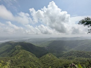 Manzaralı dağ manzarası yoğun yeşillik, bulutlu gökyüzü ve muson mevsiminde yüksek bir görüş noktasından görülebilen uzak kasaba..