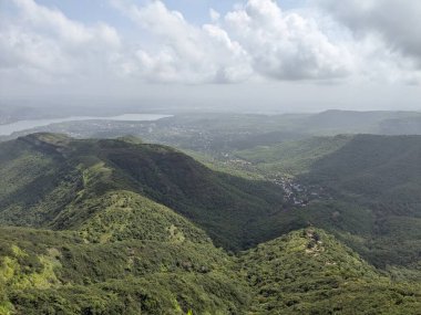 Manzaralı dağ manzarası yoğun yeşillik, bulutlu gökyüzü ve muson mevsiminde yüksek bir görüş noktasından görülebilen uzak kasaba..