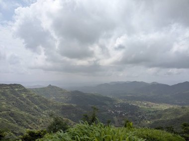 Uçsuz bucaksız yeşil bir vadinin panoramik görüntüsü sarp kayalıkları ve radyo kuleleri ile bulutlu bir muson gününde tepelik bir bölgede yakalandı..
