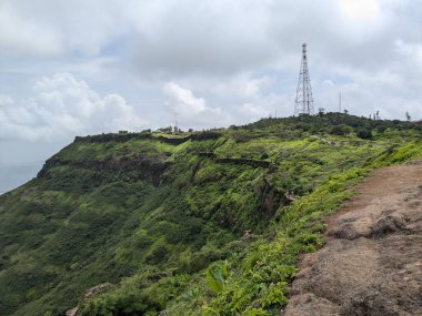 Rajgad Kalesi ve yemyeşil Sahyadri sırasının bulutlu muson yağmurlarının altında arka planda kulesi olan geniş bir manzarası.