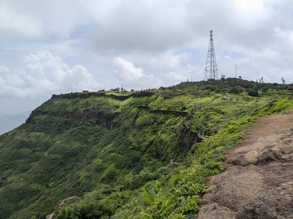 Rajgad Kalesi ve yemyeşil Sahyadri sırasının bulutlu muson yağmurlarının altında arka planda kulesi olan geniş bir manzarası.
